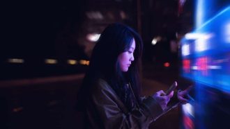 Young asian woman using touch screen in financial district at night