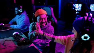 Happy Chinese gamer congratulating his friend on successful video game in entertainment club.
