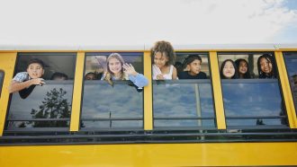 Medium wide shot of smiling middle school kids looking out open windows of school bus
